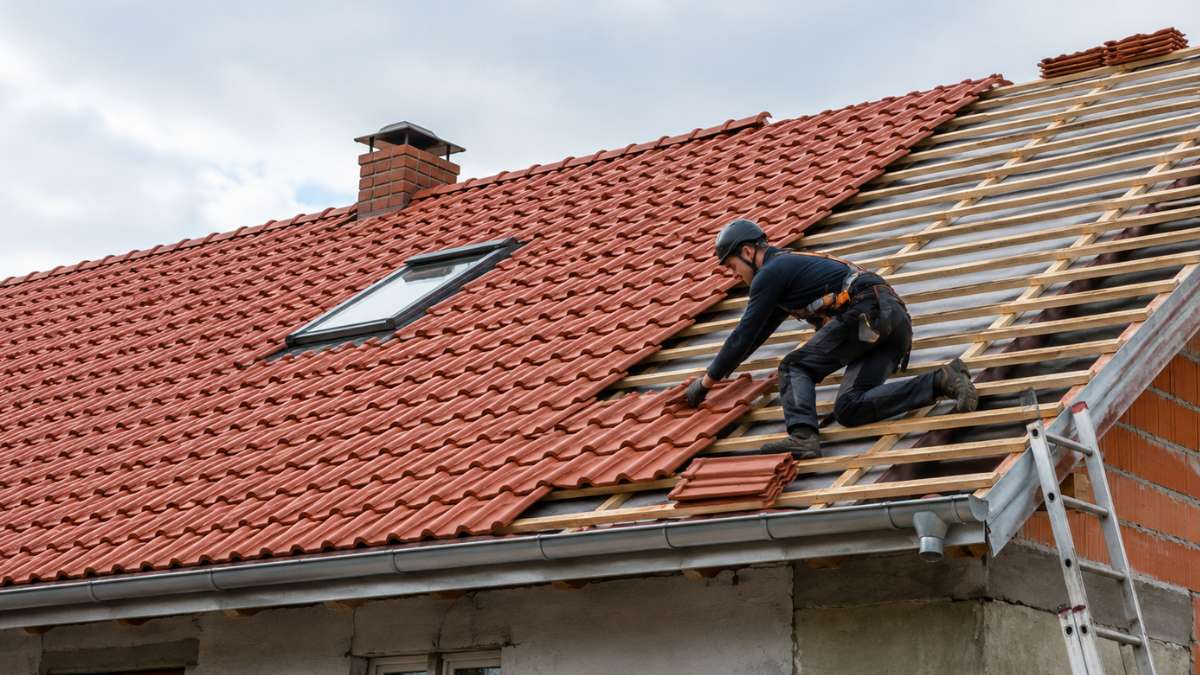 Tetőfelújítás félkész cseréptetőn dolgozó szakemberrel munkavédelmi felszerelésben
